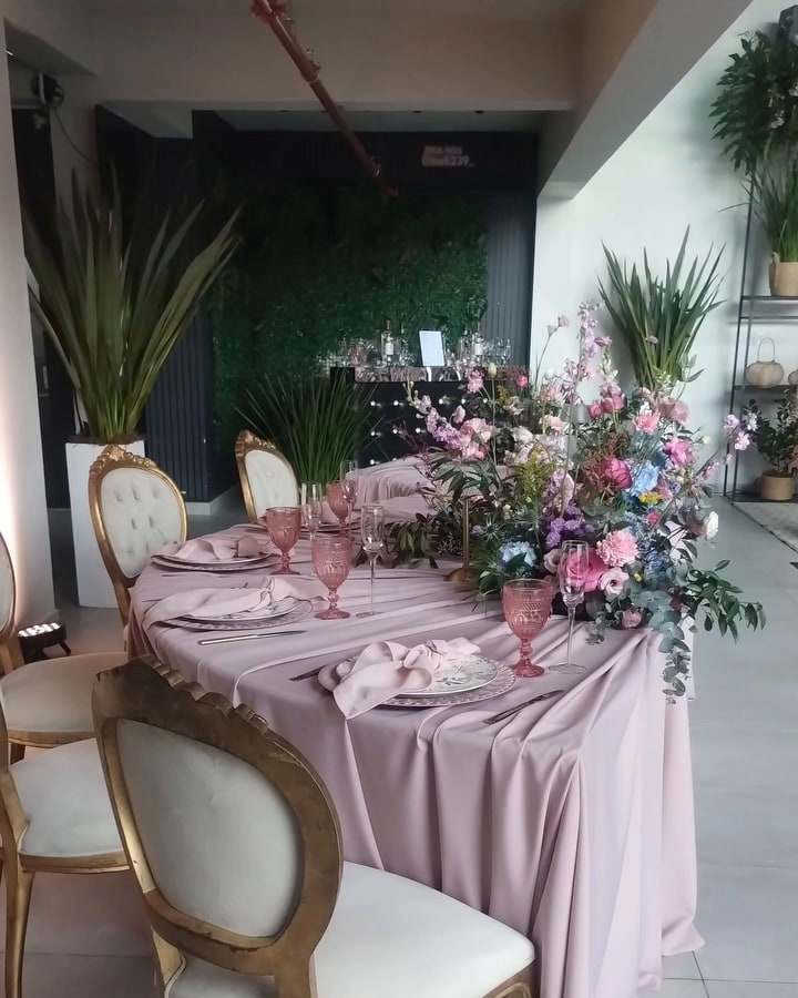 Mesa posta em tons de rosa com cadeiras medalhão e arranjos de flores para uma festa de 15 anos