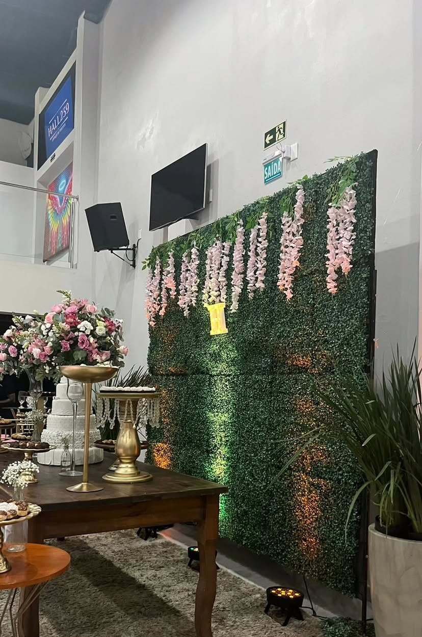Painel de folhagens com arranjos de flores brancas e mesa de madeira para festa de 15 anos