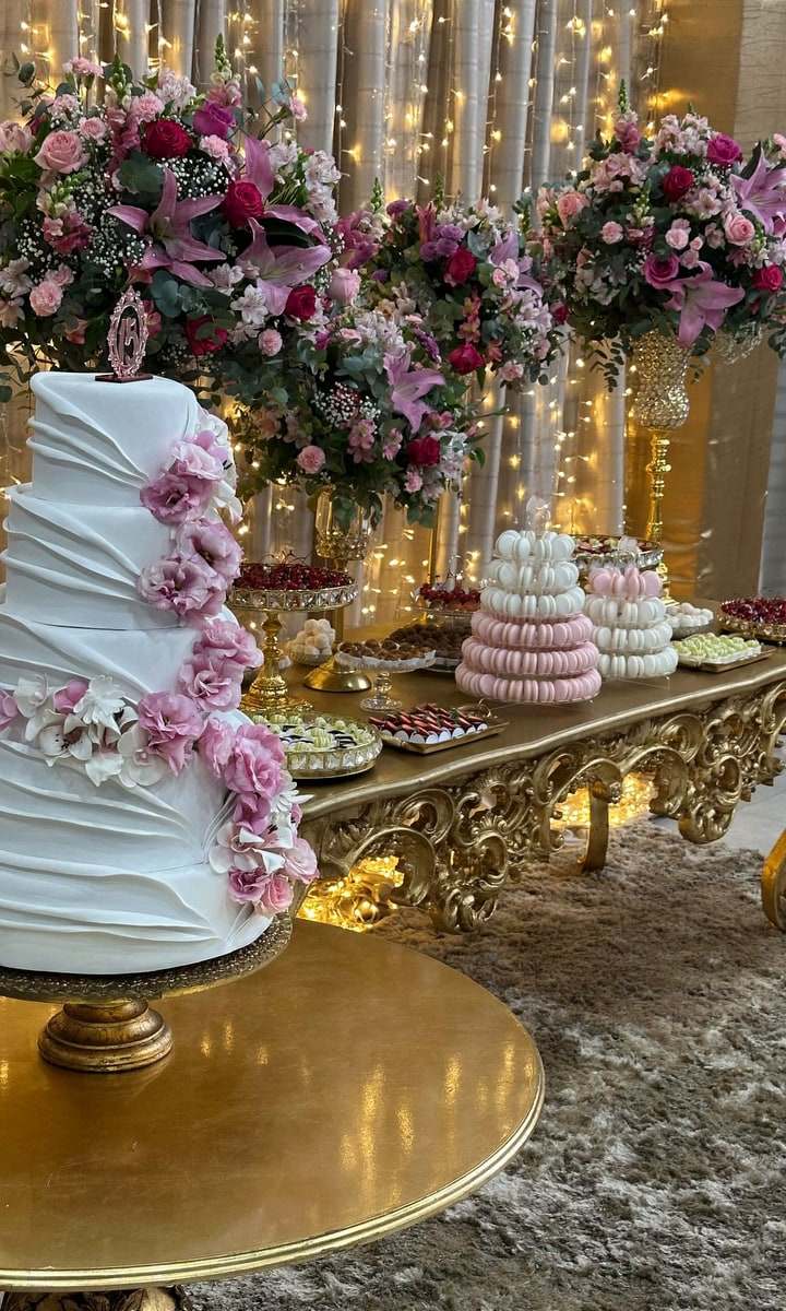 Mesa de bolo branco com flores rosas e doces sobre bandejas douradas