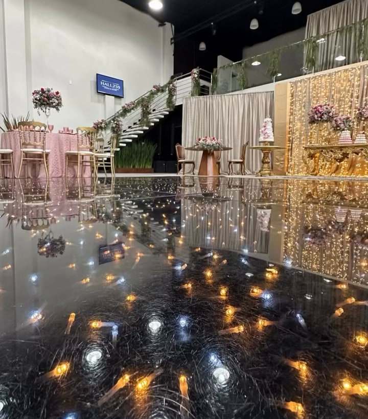 Pista de dança espelhada com reflexo das luzes, mesas decoradas e escada florida ao fundo