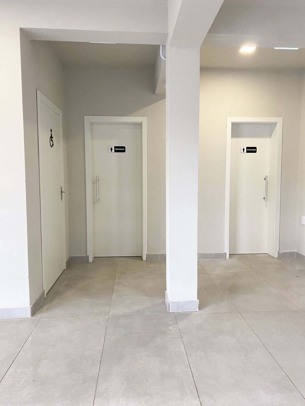 Corredor de acesso aos banheiros, com piso claro e sinalização