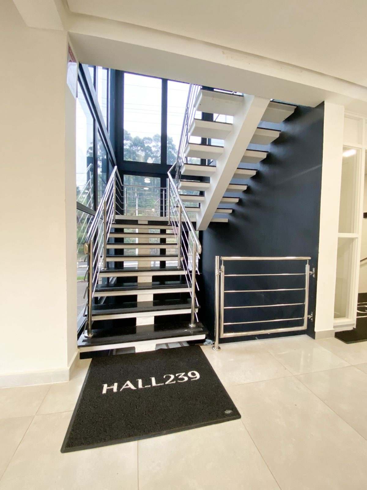 Escada vazada de inox e degraus pretos que liga o hall ao mezanino, com tapete Hall239