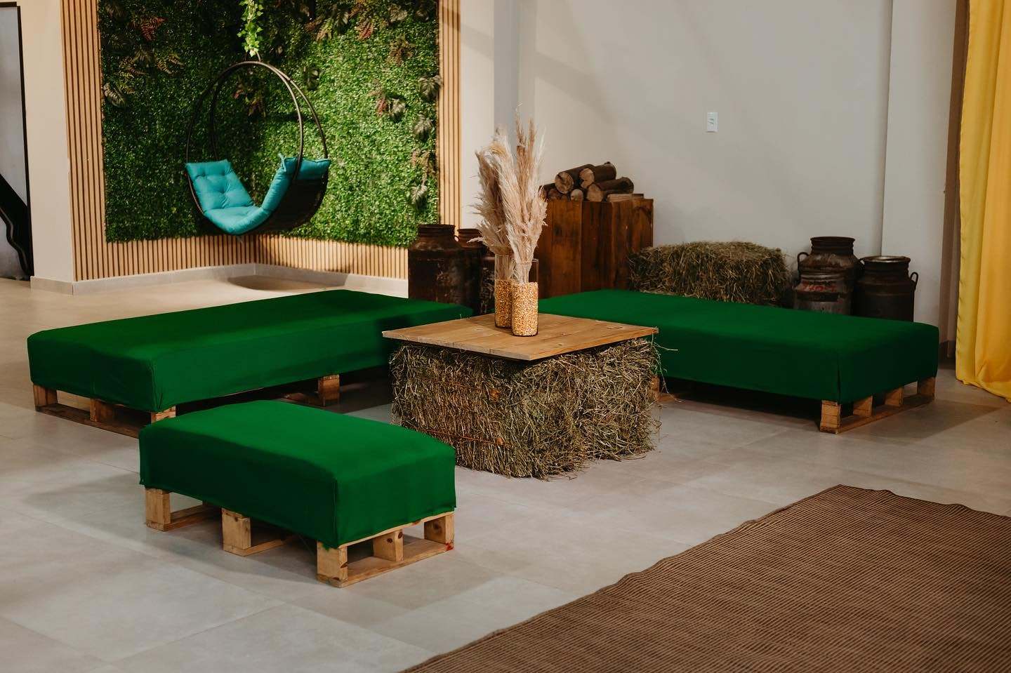 Lounge com pufes verdes e mesas de madeira ao lado do jardim vertical