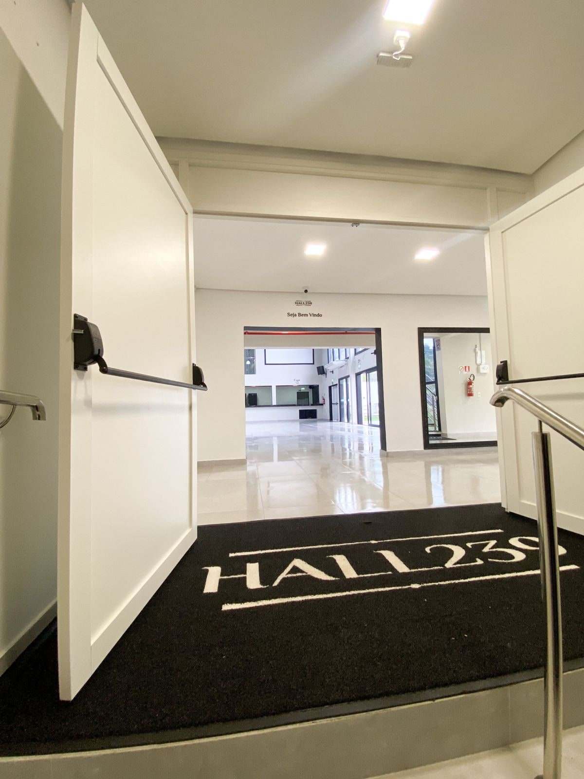 Porta principal aberta para o hall de entrada, com tapete Hall239 e o salão ao fundo
