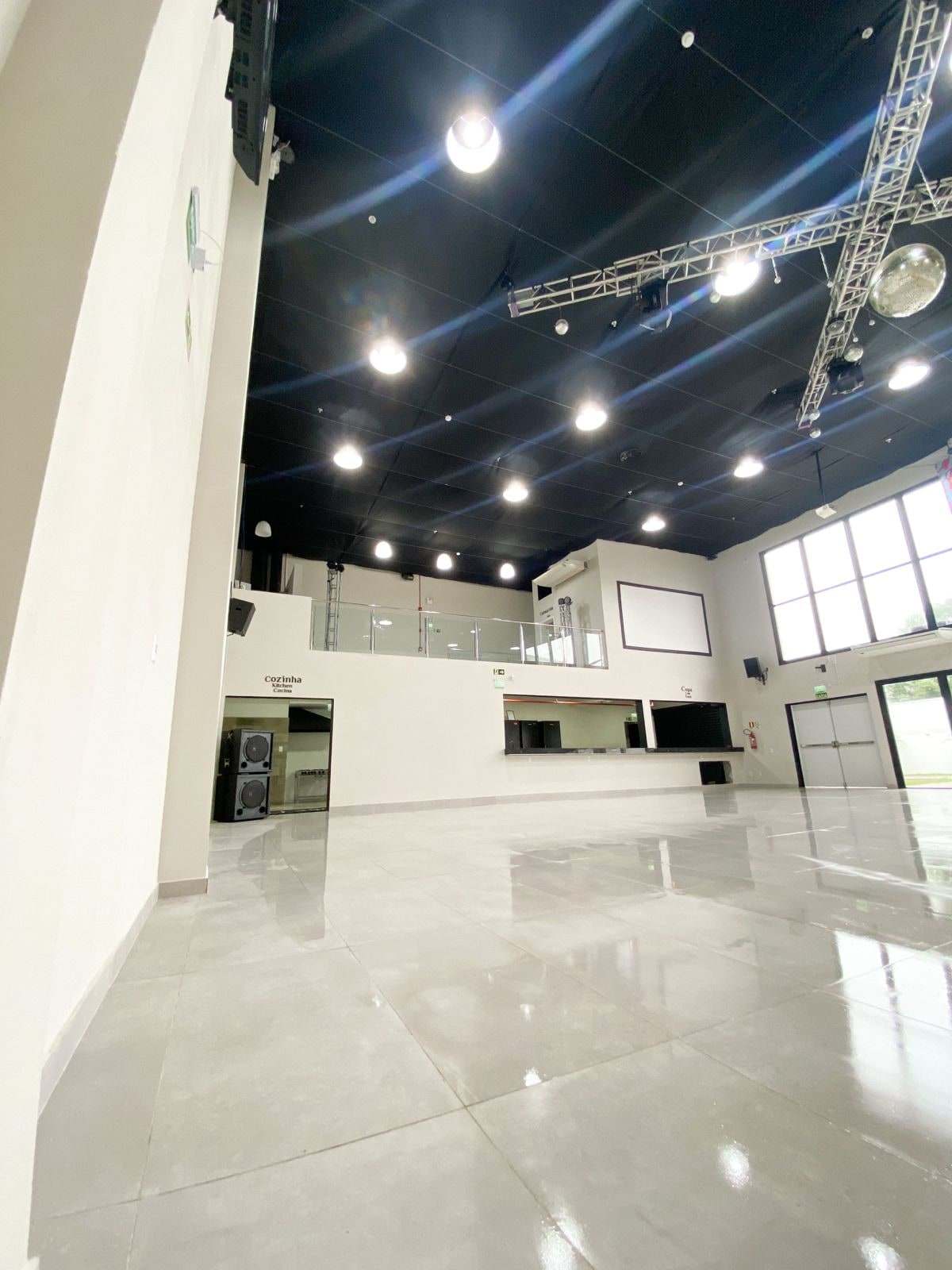 Salão principal com pé-direito alto, janelas laterais e o palco no nível superior